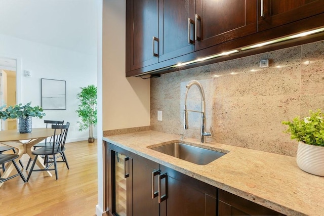 kitchen featuring a sink, light stone countertops, light wood-style floors, and dark brown cabinets