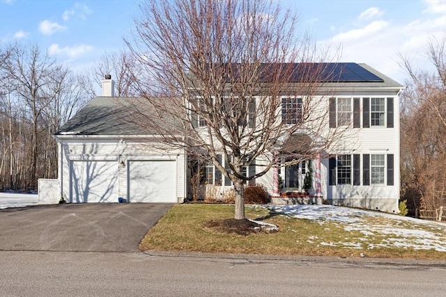 colonial-style house featuring a garage, a front yard, and solar panels