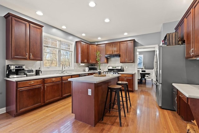 kitchen with sink, light wood-type flooring, appliances with stainless steel finishes, a kitchen island, and a kitchen bar