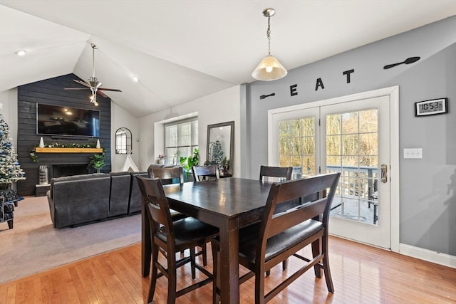 dining room featuring ceiling fan, a large fireplace, light wood-type flooring, and lofted ceiling