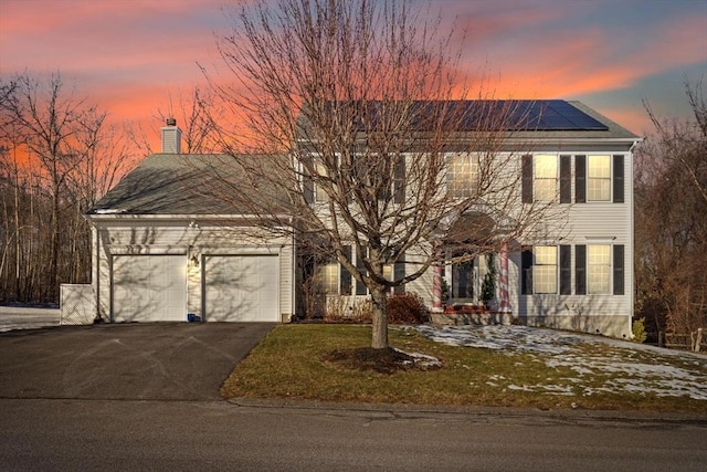 colonial inspired home with a lawn, solar panels, and a garage