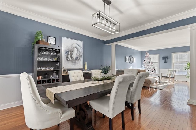 dining space with decorative columns, wood-type flooring, and ornamental molding