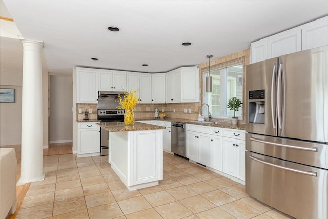 kitchen with white cabinets, dark stone countertops, a kitchen island, stainless steel appliances, and decorative columns