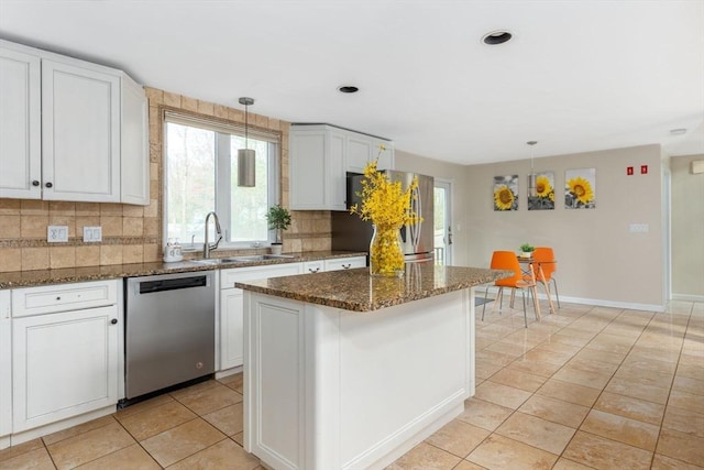 kitchen featuring stainless steel appliances, sink, dark stone countertops, a center island, and hanging light fixtures