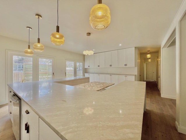 kitchen featuring hardwood / wood-style flooring, light stone countertops, white cabinets, decorative light fixtures, and a spacious island