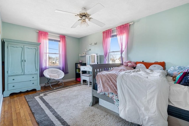 bedroom with hardwood / wood-style flooring, a ceiling fan, baseboards, and a textured ceiling