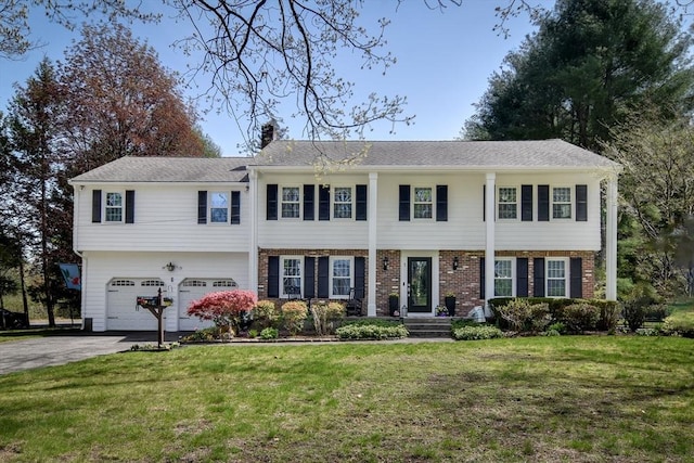 view of front of property with driveway, a chimney, brick siding, a front lawn, and an attached garage
