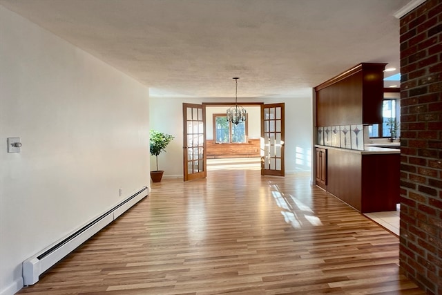 unfurnished dining area featuring baseboard heating, a textured ceiling, an inviting chandelier, light hardwood / wood-style flooring, and french doors