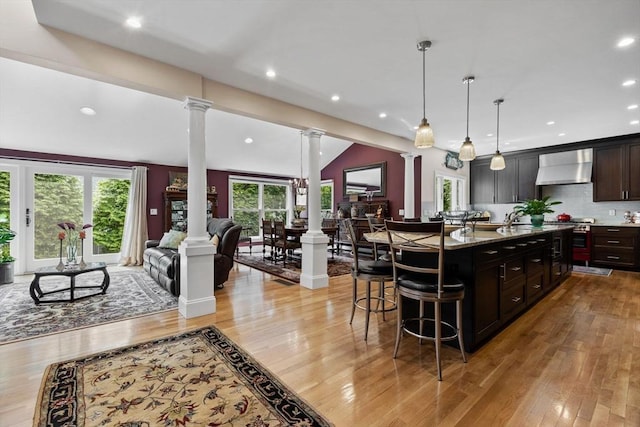 1488 Washington St Unit 1488, Newton, MA 02465 - kitchen featuring decorative columns, wall chimney exhaust hood, a kitchen breakfast bar, light wood-style floors, and recessed lighting