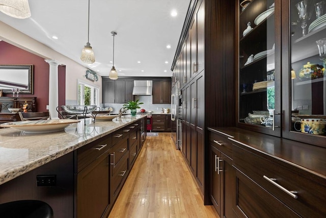 1488 Washington St Unit 1488, Newton, MA 02465 - kitchen featuring extractor fan, light wood finished floors, dark brown cabinets, ornate columns, and pendant lighting