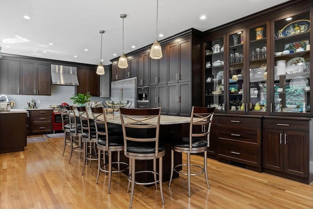 1488 Washington St Unit 1488, Newton, MA 02465 - kitchen featuring high quality appliances, wall chimney exhaust hood, light wood-style floors, dark brown cabinets, and recessed lighting