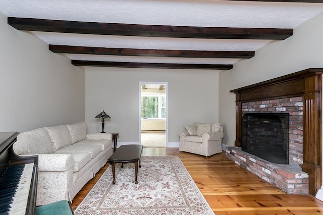 living area featuring beamed ceiling, a brick fireplace, and wood finished floors