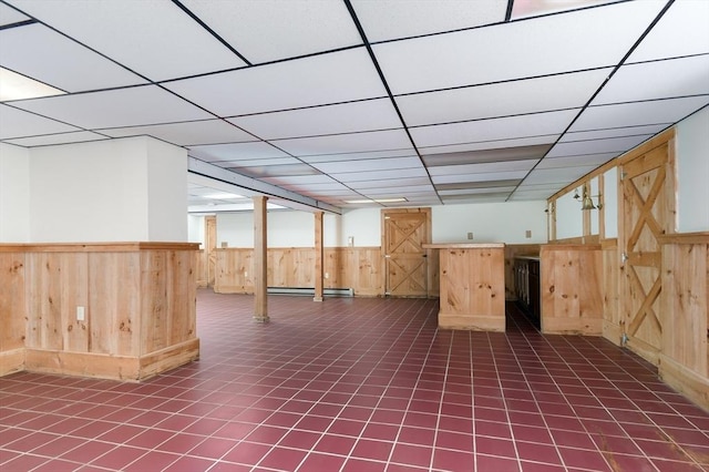 basement with wood walls, a baseboard heating unit, wainscoting, and a paneled ceiling