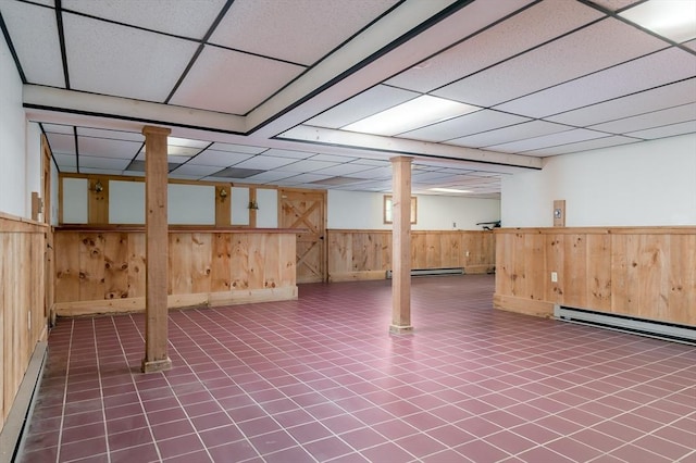 finished below grade area with a drop ceiling, a wainscoted wall, a baseboard radiator, wood walls, and tile patterned floors
