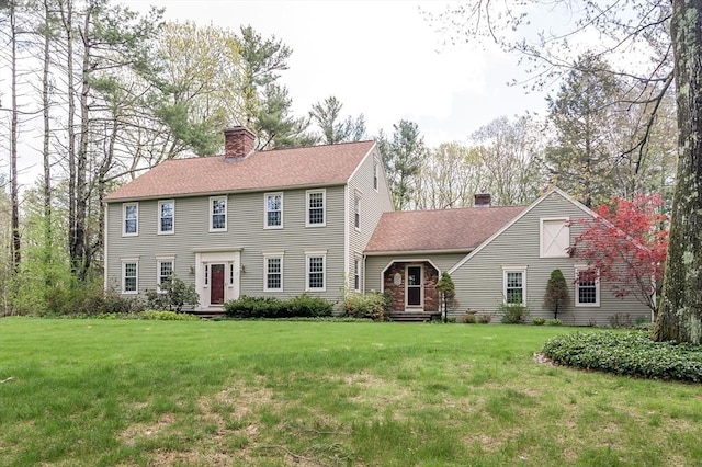 colonial-style house with a chimney, a front lawn, and a shingled roof