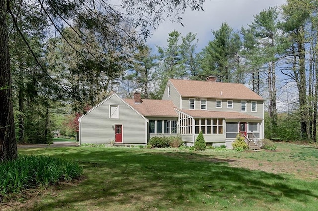 back of property featuring a sunroom, a chimney, a lawn, and a shingled roof