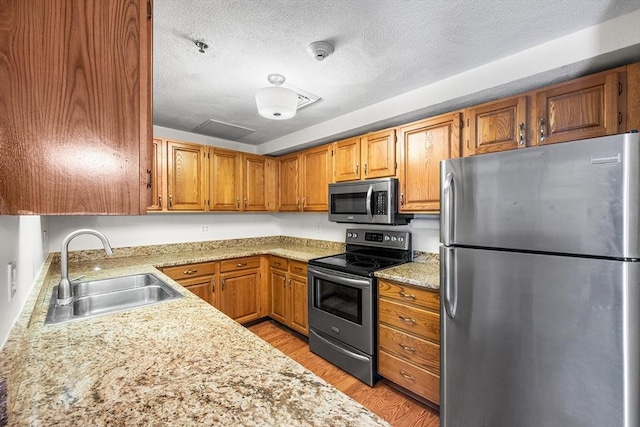 39 Parlin St Unit 503, Everett, MA 02149 - kitchen with stainless steel appliances, a sink, brown cabinets, light wood-type flooring, and a textured ceiling