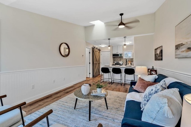 81 Fletcher Ln Unit I, Brewster, MA 02631 - living area featuring a barn door, light wood-style flooring, a wainscoted wall, and a ceiling fan