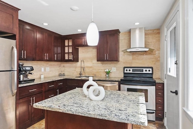 kitchen featuring light stone countertops, decorative backsplash, appliances with stainless steel finishes, wall chimney exhaust hood, and a sink