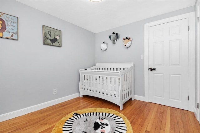 bedroom with a nursery area, light wood-style flooring, and baseboards