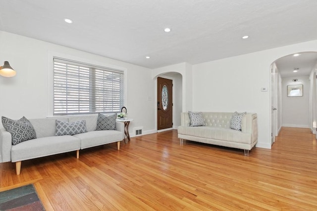 living area featuring recessed lighting, visible vents, arched walkways, and light wood-style floors