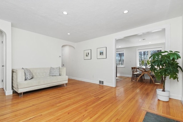 living area with visible vents, light wood-style flooring, baseboards, and arched walkways