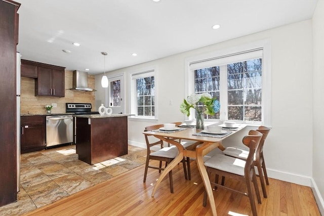 kitchen featuring a center island, dark brown cabinetry, appliances with stainless steel finishes, wall chimney range hood, and decorative backsplash