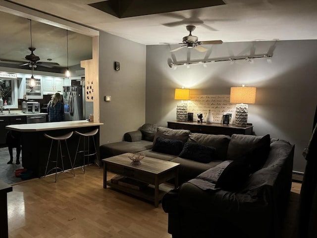 living room featuring hardwood / wood-style flooring, ceiling fan, sink, and a baseboard heating unit