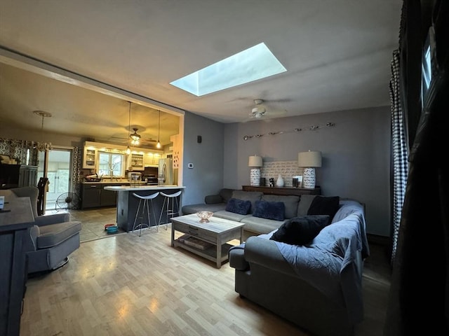 living room featuring light wood-type flooring, a skylight, and ceiling fan