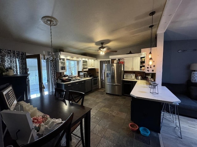 kitchen featuring kitchen peninsula, a kitchen breakfast bar, stainless steel appliances, white cabinetry, and hanging light fixtures