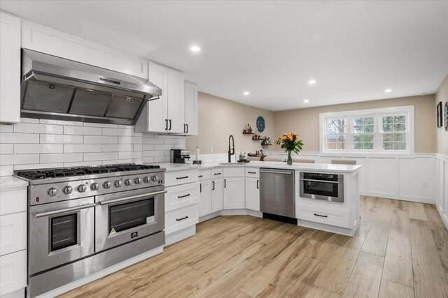 12 Salem St Unit 2, Haverhill, MA 01835 - kitchen featuring light countertops, a peninsula, light wood finished floors, stainless steel appliances, and wall chimney range hood