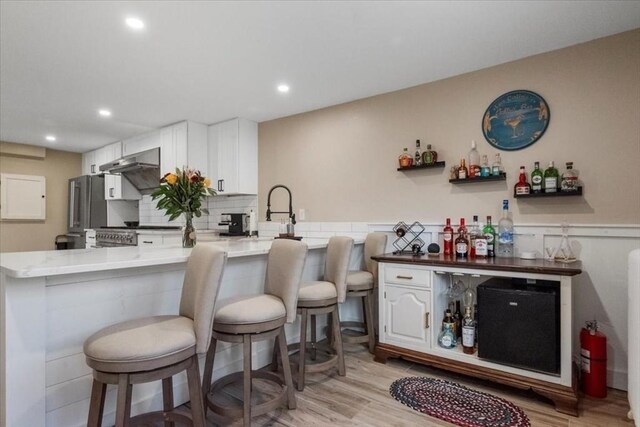 12 Salem St Unit 2, Haverhill, MA 01835 - kitchen featuring white cabinetry, a breakfast bar area, decorative backsplash, light wood-style flooring, and a peninsula