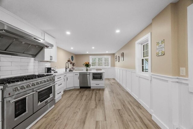 12 Salem St Unit 2, Haverhill, MA 01835 - kitchen featuring stainless steel appliances, a sink, white cabinets, a peninsula, and wall chimney exhaust hood