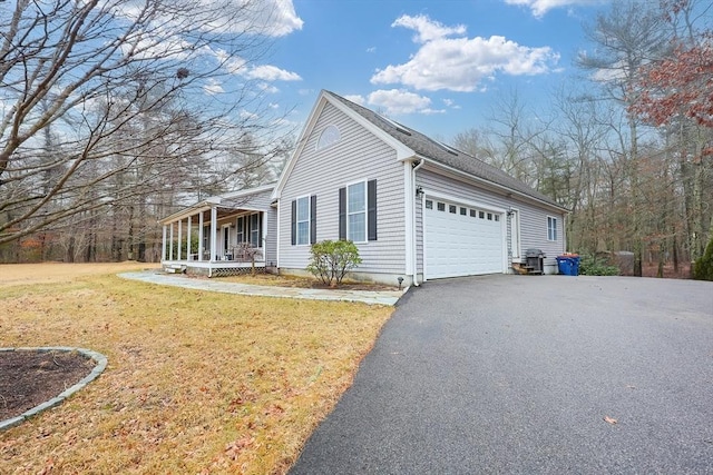 view of side of home with a garage, covered porch, driveway, and a lawn