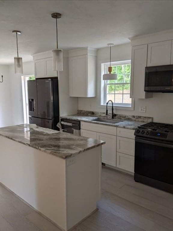 kitchen featuring appliances with stainless steel finishes, sink, a center island, hanging light fixtures, and white cabinetry