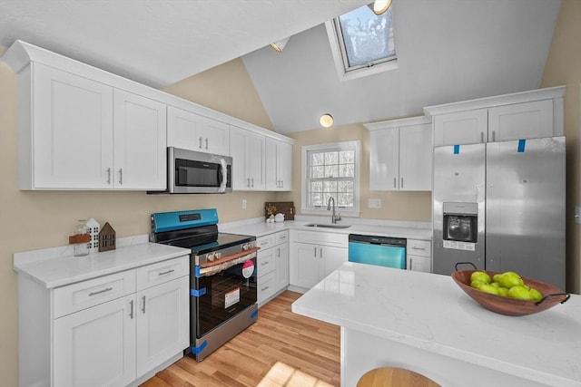 kitchen featuring lofted ceiling with skylight, sink, white cabinets, stainless steel appliances, and light wood-type flooring