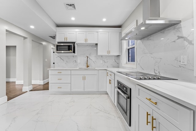 kitchen with stainless steel appliances, light stone counters, white cabinets, wall chimney exhaust hood, and sink