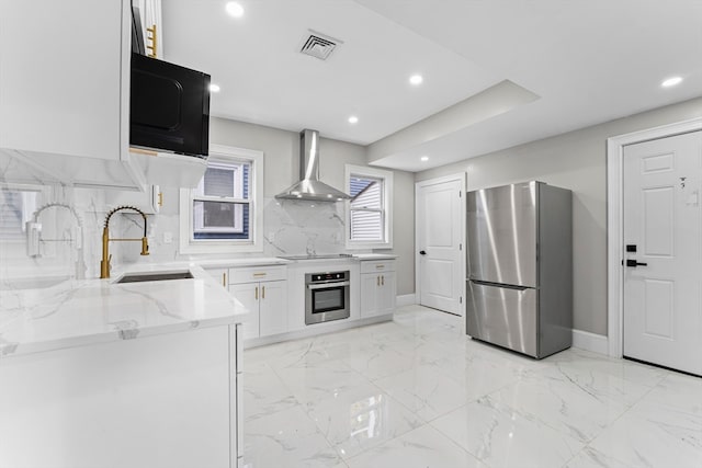 kitchen featuring light stone counters, appliances with stainless steel finishes, sink, white cabinets, and wall chimney exhaust hood