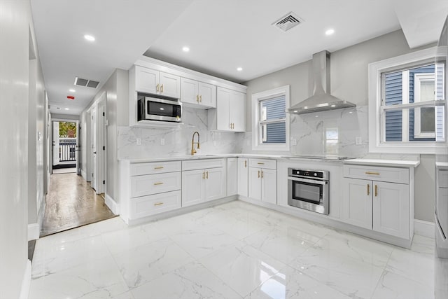 kitchen featuring stainless steel appliances, white cabinetry, wall chimney range hood, backsplash, and sink