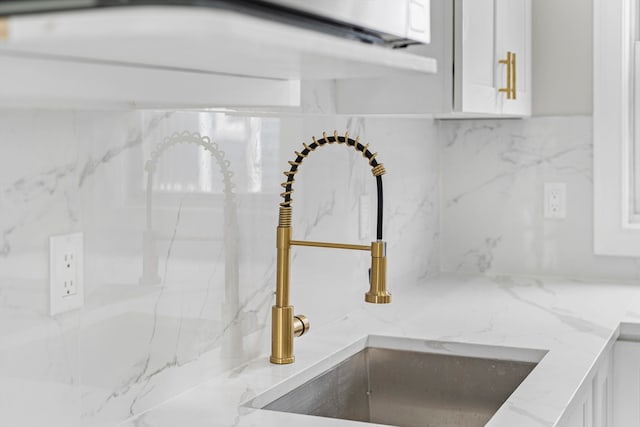 interior details featuring white cabinetry, sink, and light stone counters