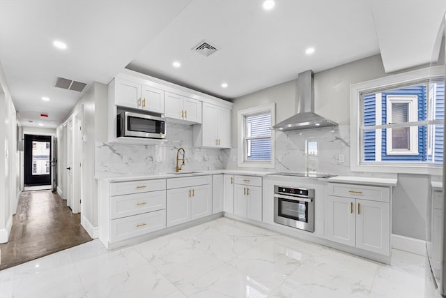 kitchen with stainless steel appliances, white cabinets, sink, tasteful backsplash, and wall chimney range hood