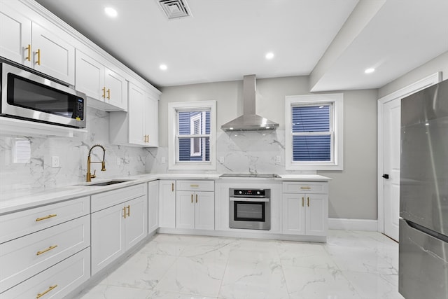 kitchen featuring stainless steel appliances, white cabinets, decorative backsplash, sink, and wall chimney range hood