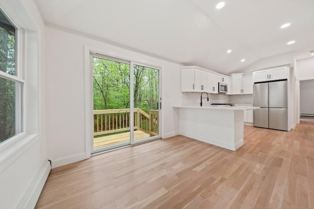 kitchen with a peninsula, backsplash, light countertops, white cabinets, and appliances with stainless steel finishes