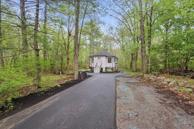 exterior space featuring aphalt driveway, a forest view, and a chimney