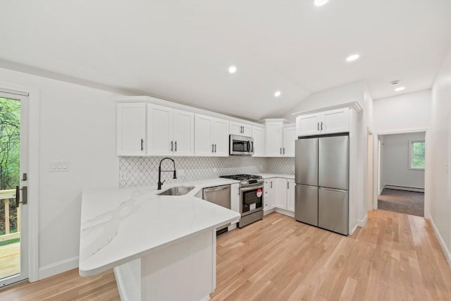 kitchen featuring a peninsula, a sink, white cabinetry, backsplash, and appliances with stainless steel finishes