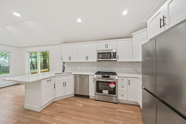 kitchen featuring stainless steel appliances, light wood finished floors, a sink, a peninsula, and light countertops