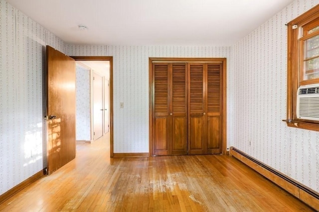 unfurnished bedroom featuring baseboard heating, a closet, and light hardwood / wood-style floors