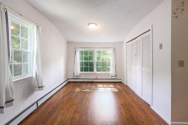 unfurnished bedroom with dark hardwood / wood-style floors, baseboard heating, and multiple windows