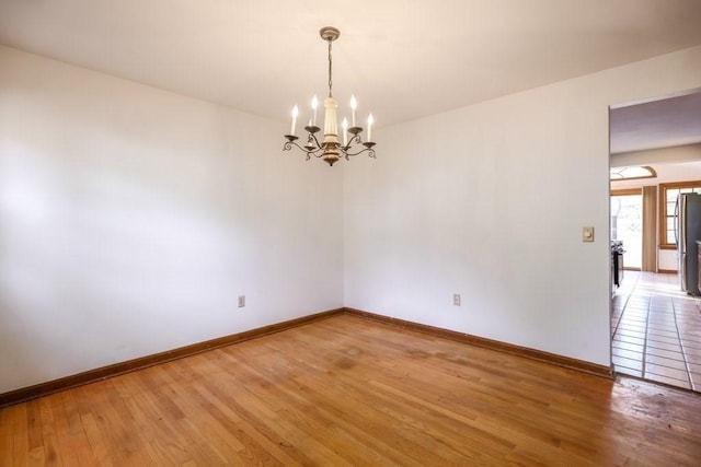 spare room with wood-type flooring and an inviting chandelier