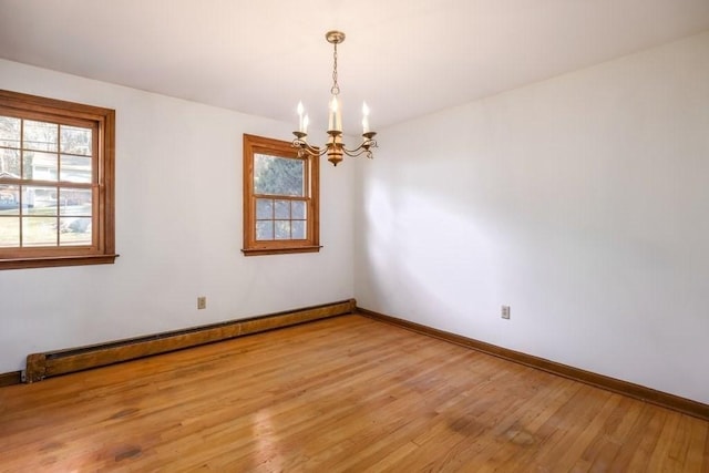 empty room featuring wood-type flooring, a baseboard heating unit, and a notable chandelier